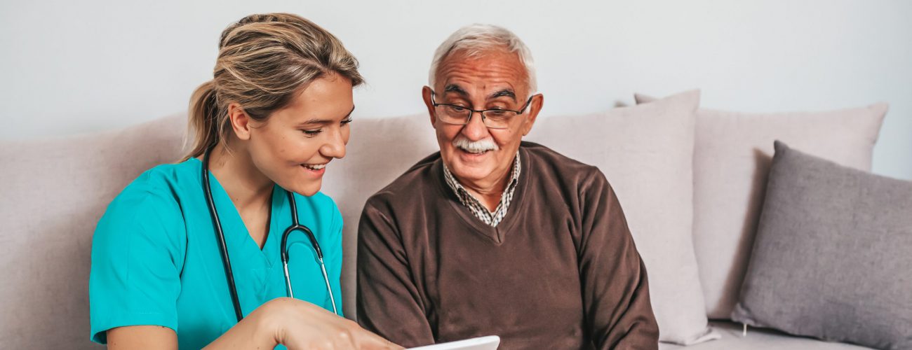 Health visitor and a senior man during home visit. Photo of at home nurse showing test results to a senior man on a tablet.