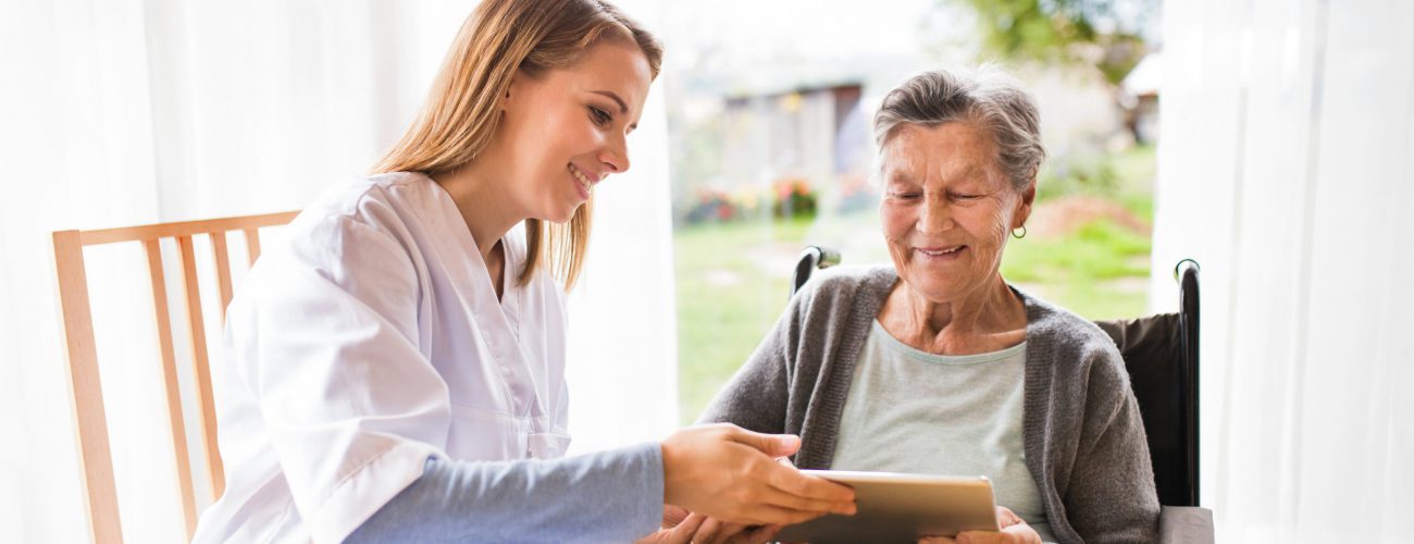Home health aide and a senior woman with tablet during home visit.